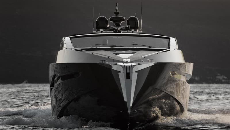A dark motor yacht seen head-on as it moves through the water.
