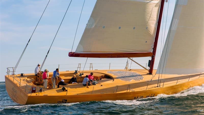 Crew sailing a wooden yacht beneath cream-colored sails.