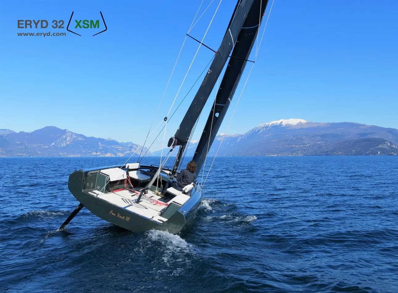 Sailboat heeling across blue water with mountains in the distance.
